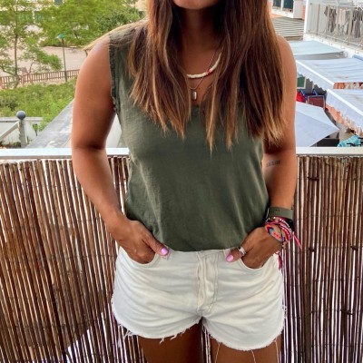 Pessoa de t-shirt verde-oliva sem mangas e shorts brancos na varanda com cerca de bambu