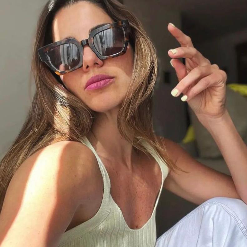 Mulher com óculos de sol e top branco num fundo interior