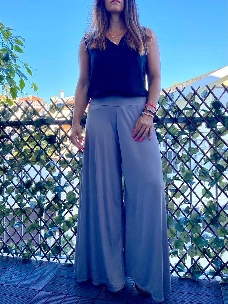 Mulher com top preto e calças largas cinza em varanda com plantas