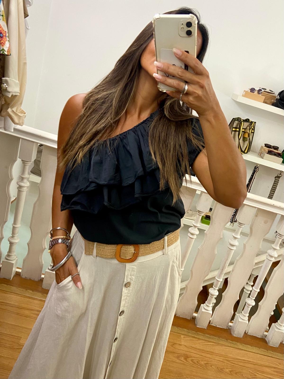 Pessoa a tirar selfie com top preto folhos e saia clara longa com cinto bege, em interior com escada branca