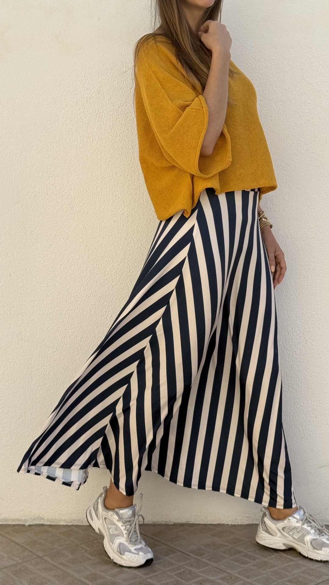 Modelo com camisola mostarda de malha e saia longa com riscas pretas e brancas usando ténis brancos prateados