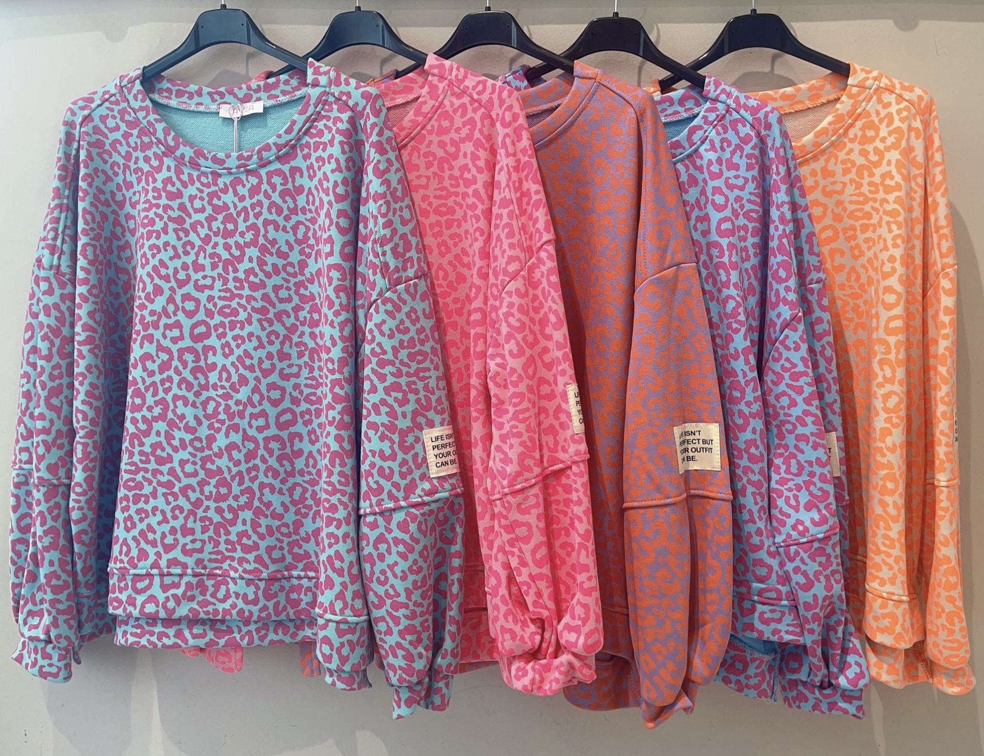 Cinco sweatshirts coloridas com padrão de leopardo penduradas em cabides pretos