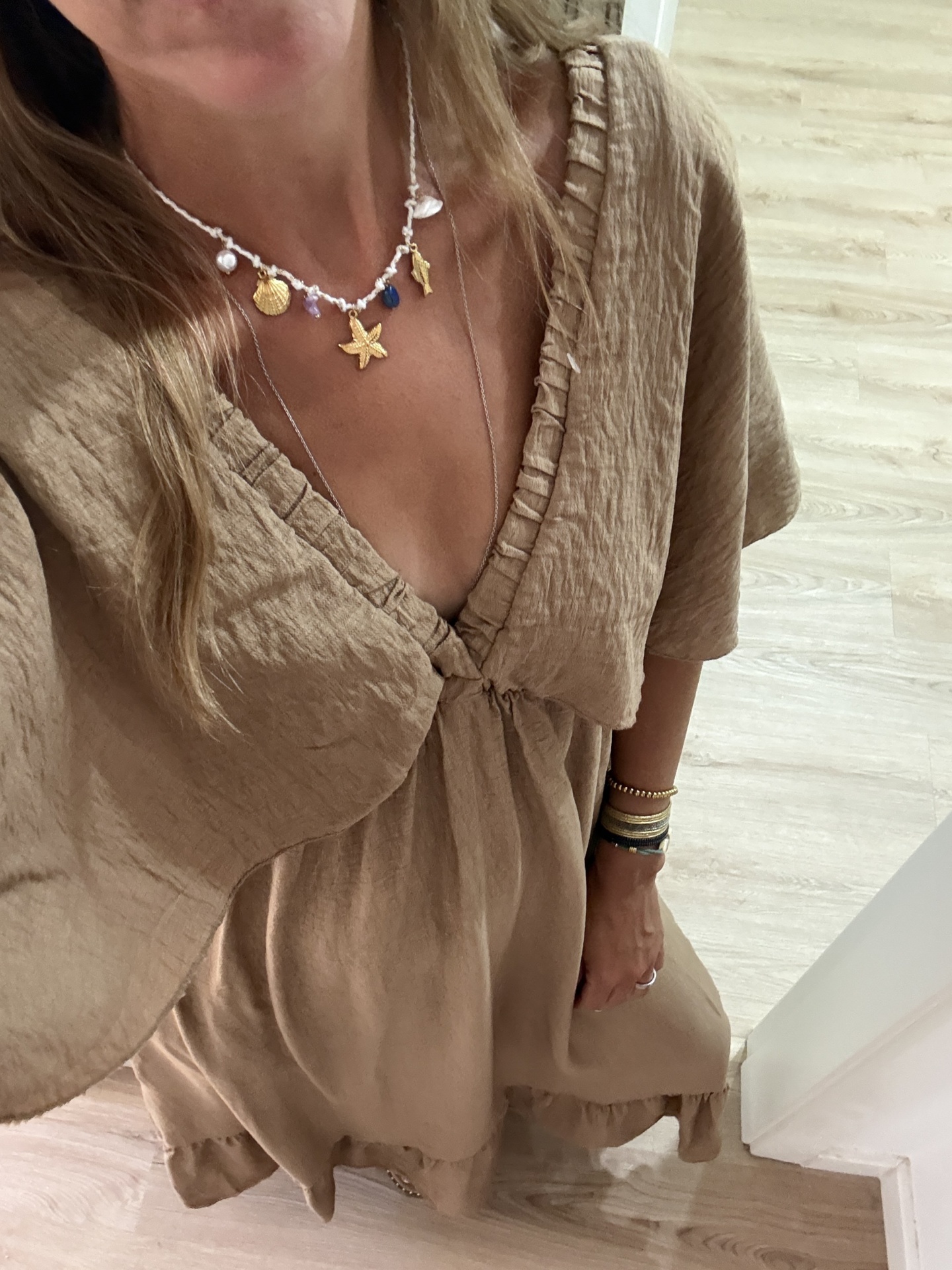 Vestido castanho claro com textura amassada e colar com pendentes dourados e azuis