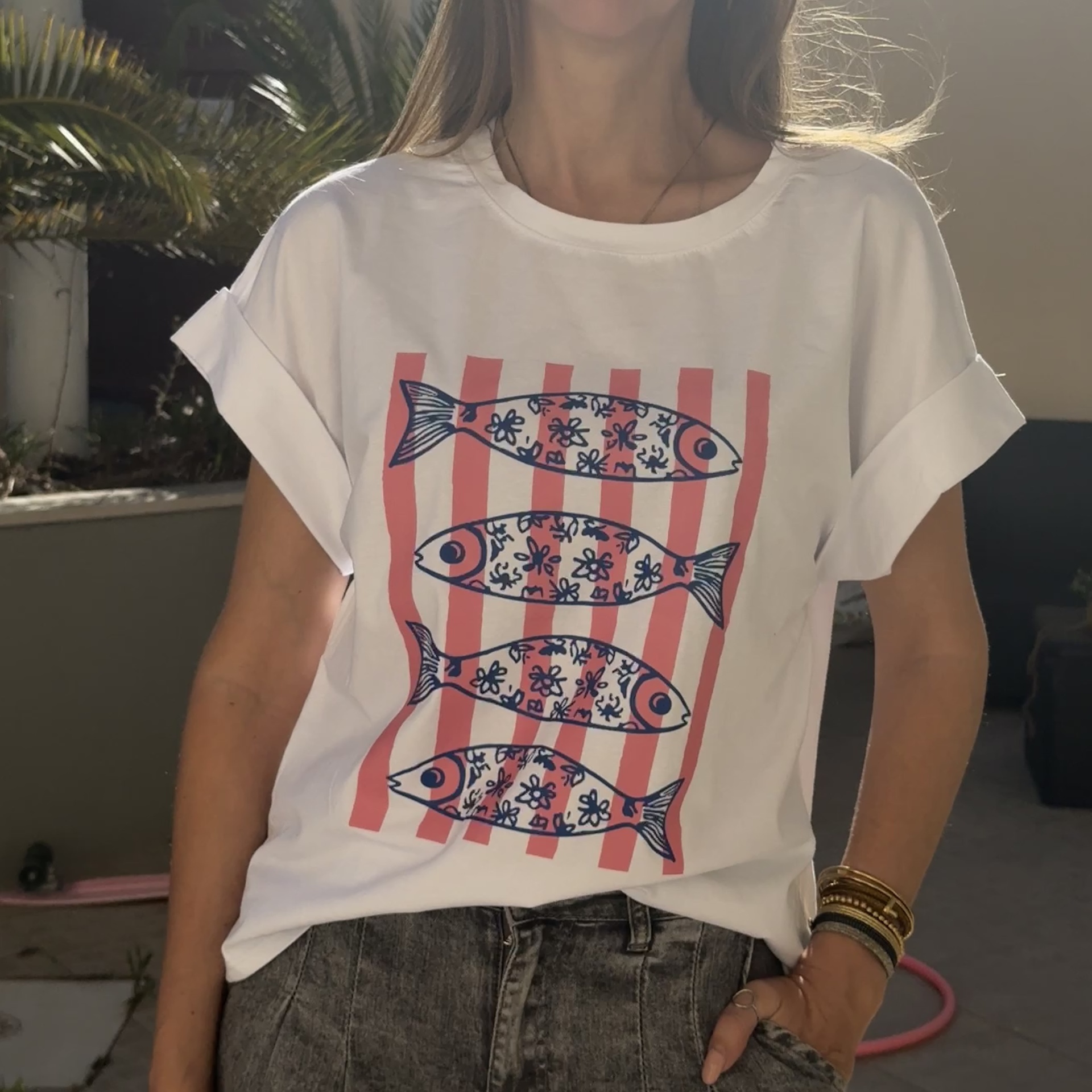 T-shirt branca com estampa de peixes azuis e rosa, com calças de ganga cinza ao ar livre