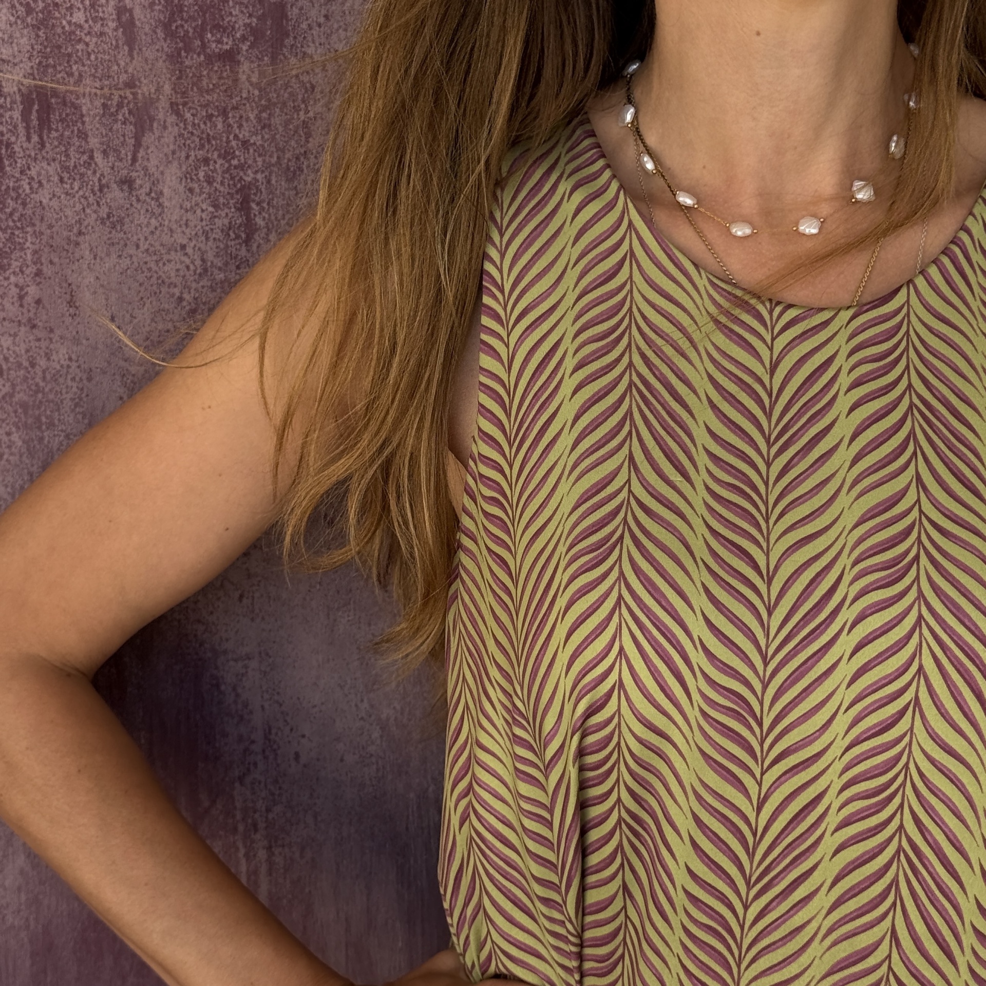 Blusa com padrão folhas verdes e roxas, colares de pérolas e fundo roxo