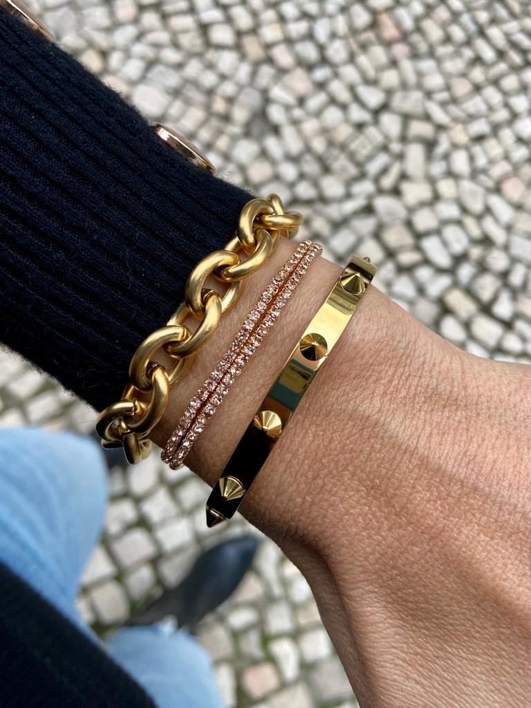 Pulso com três pulseiras douradas e brilhantes sobre calçada de pedras
