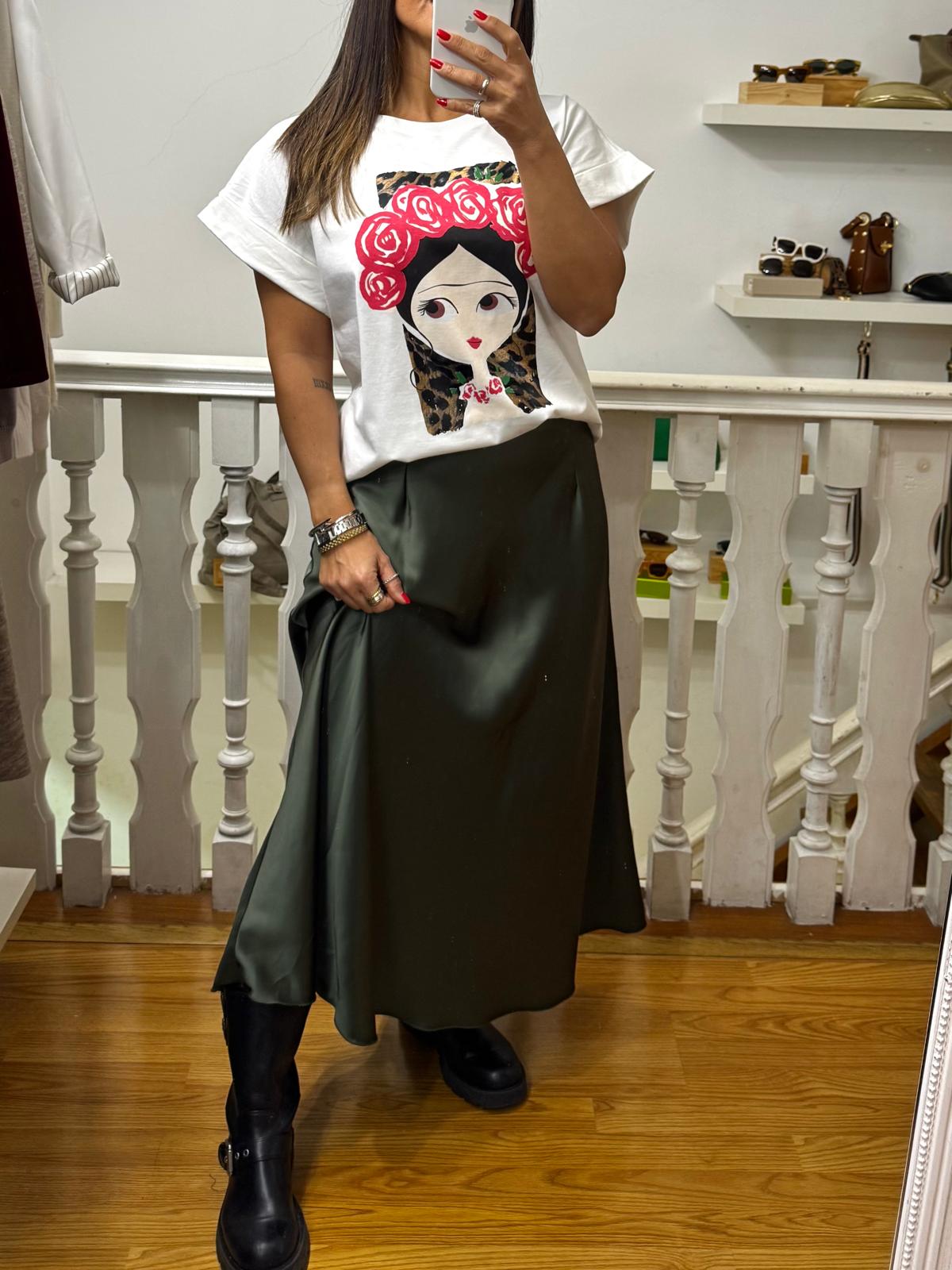 Mulher com t-shirt branca estampada, saia verde escura e botas pretas em ambiente interno
