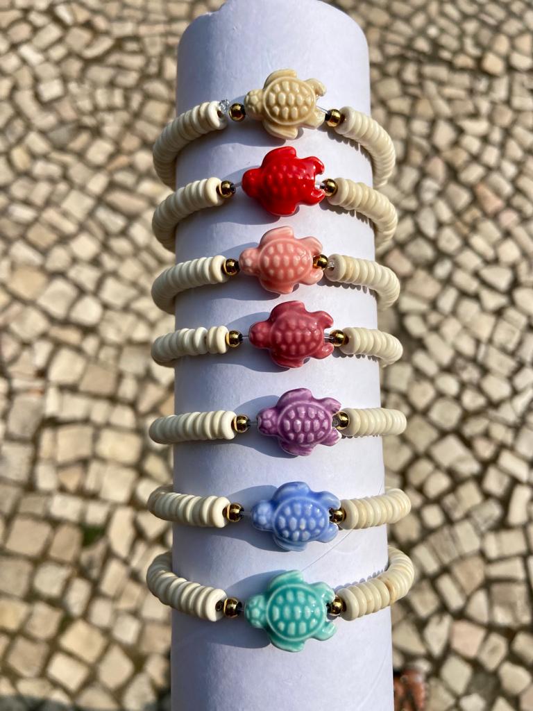 Pulseiras com contas em forma de tartaruga coloridas sobre suporte branco cilindrico