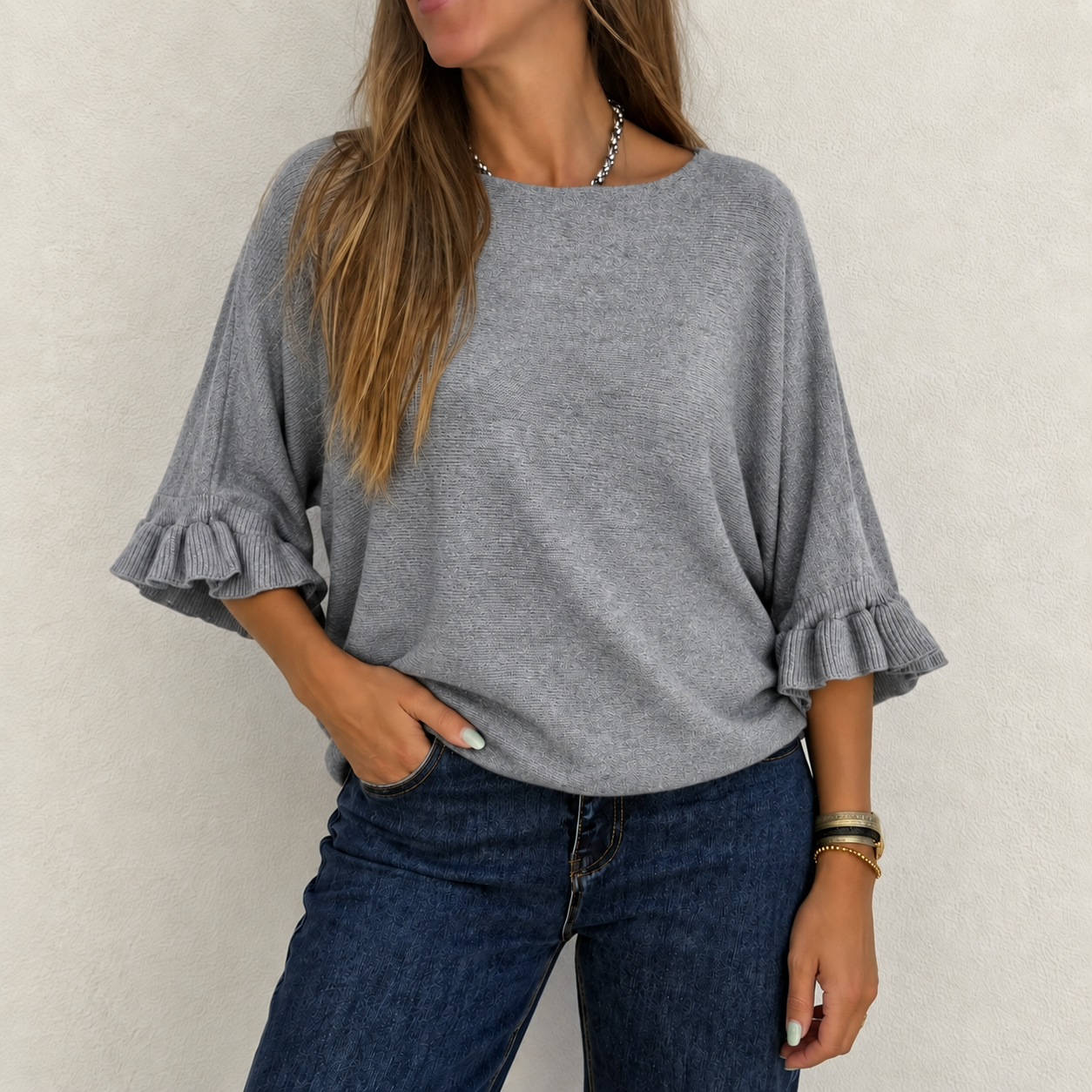 Mulher veste camisola cinzenta de malha com folhos e calças de ganga
