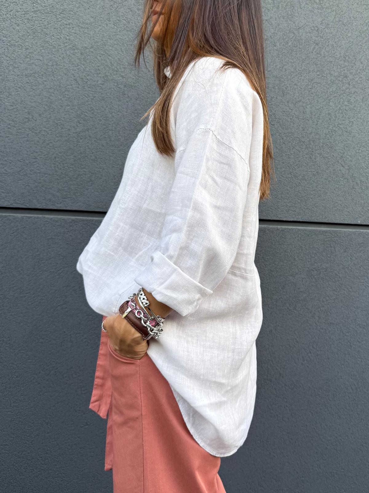 Pessoa de lado vestindo camisa branca de linho e calças cor de salmão com pulseiras prateadas