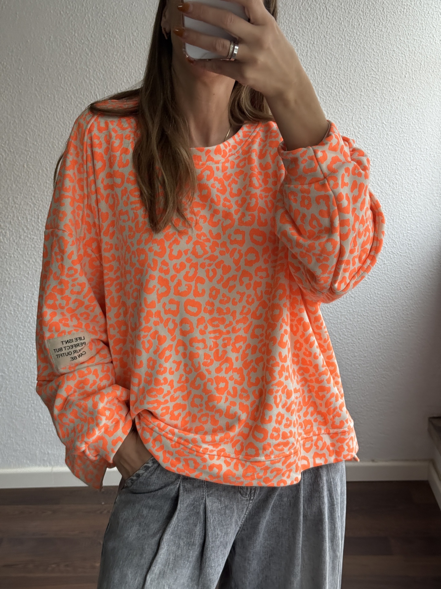 Sweatshirt feminina laranja com padrão animal print bege e etiqueta com texto na manga esquerda