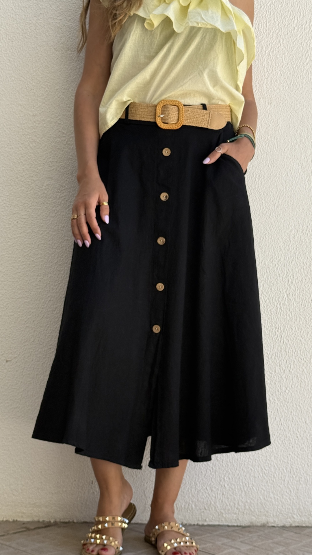 Saia midi preta com botões, cinto castanho, camisola amarela, sandálias douradas com tachas.