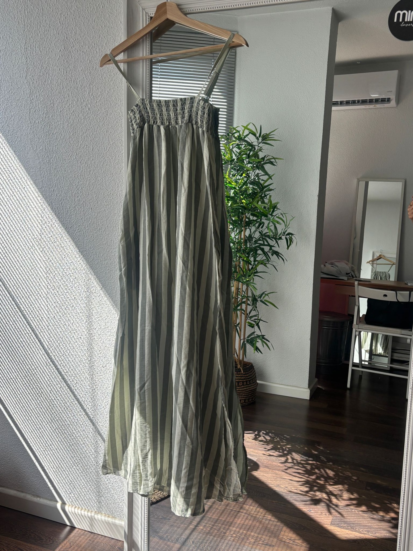 Vestido comprido com riscas verticais verdes e bege pendurado num cabide de madeira
