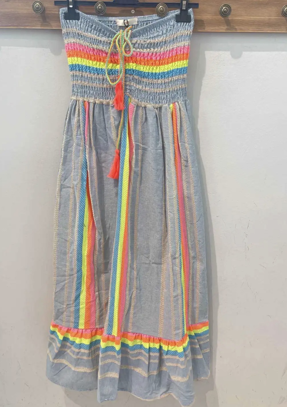 Vestido longo azul claro com riscas verticais coloridas e cordões com pompons.