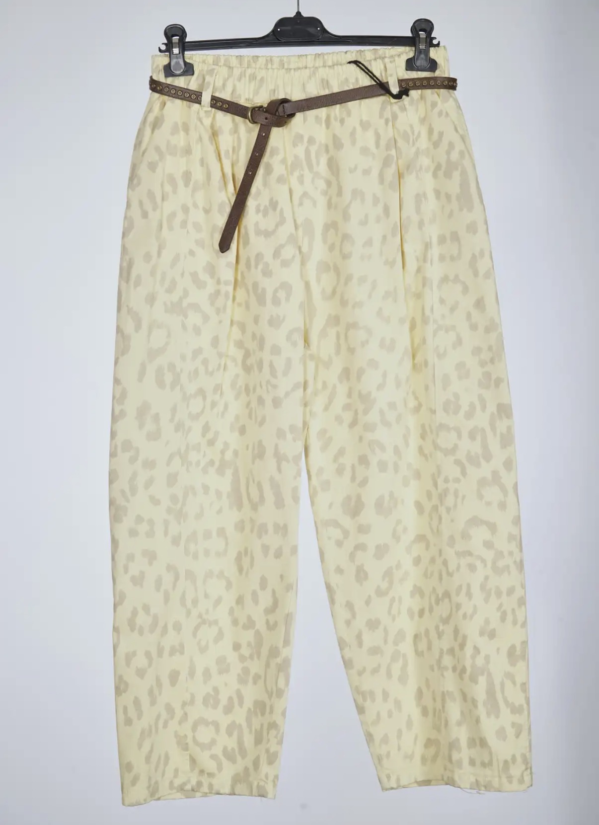 Calças beige com padrão animal print e cinto castanho penduradas num cabide preto