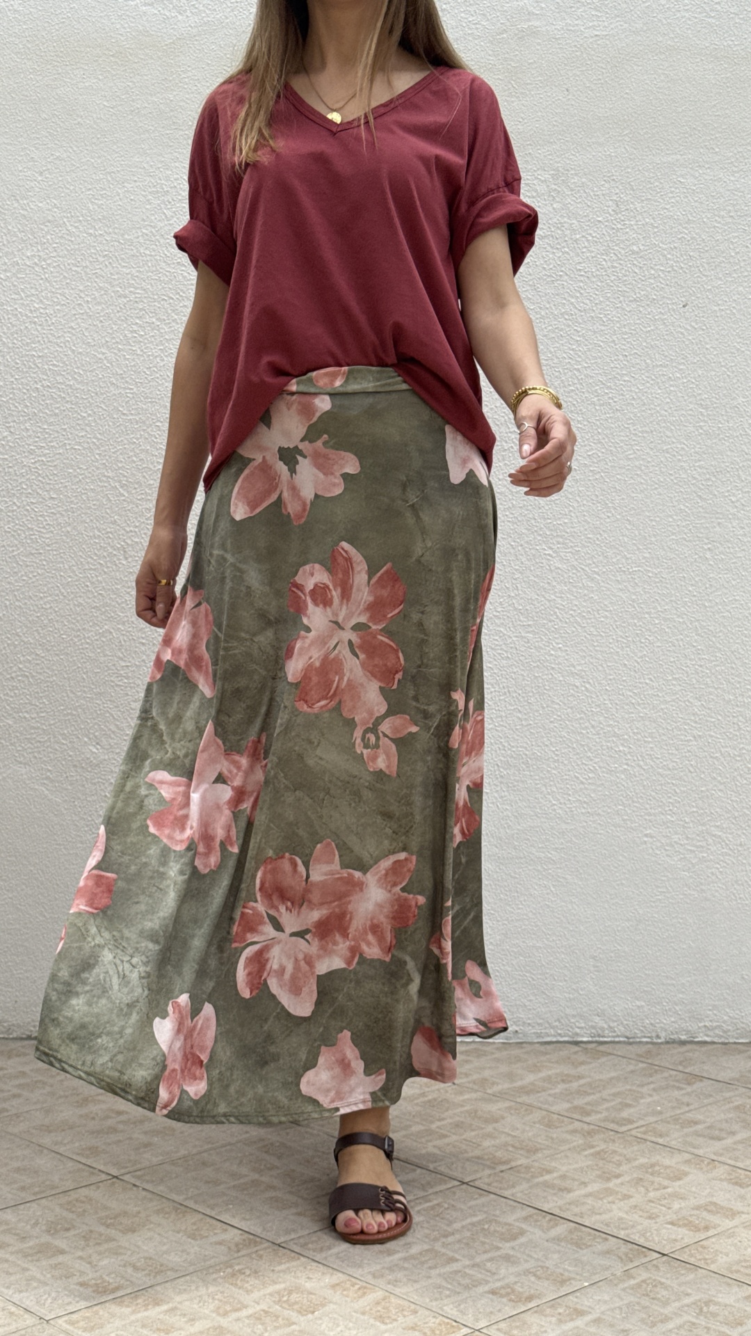 Pessoa de saia comprida floral verde e rosa e t-shirt bordeaux com sandálias