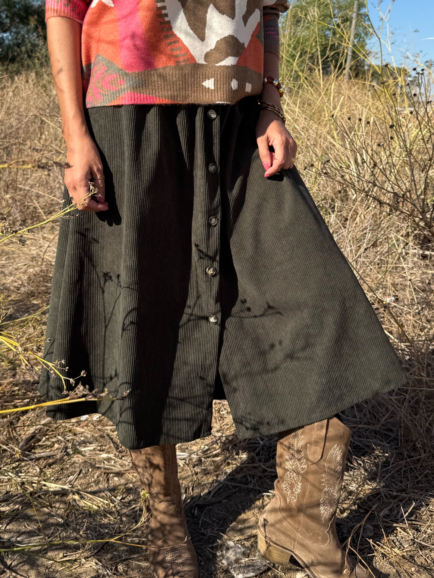 Saia midi preta com botões e botas castanhas bordadas em ambiente exterior seco