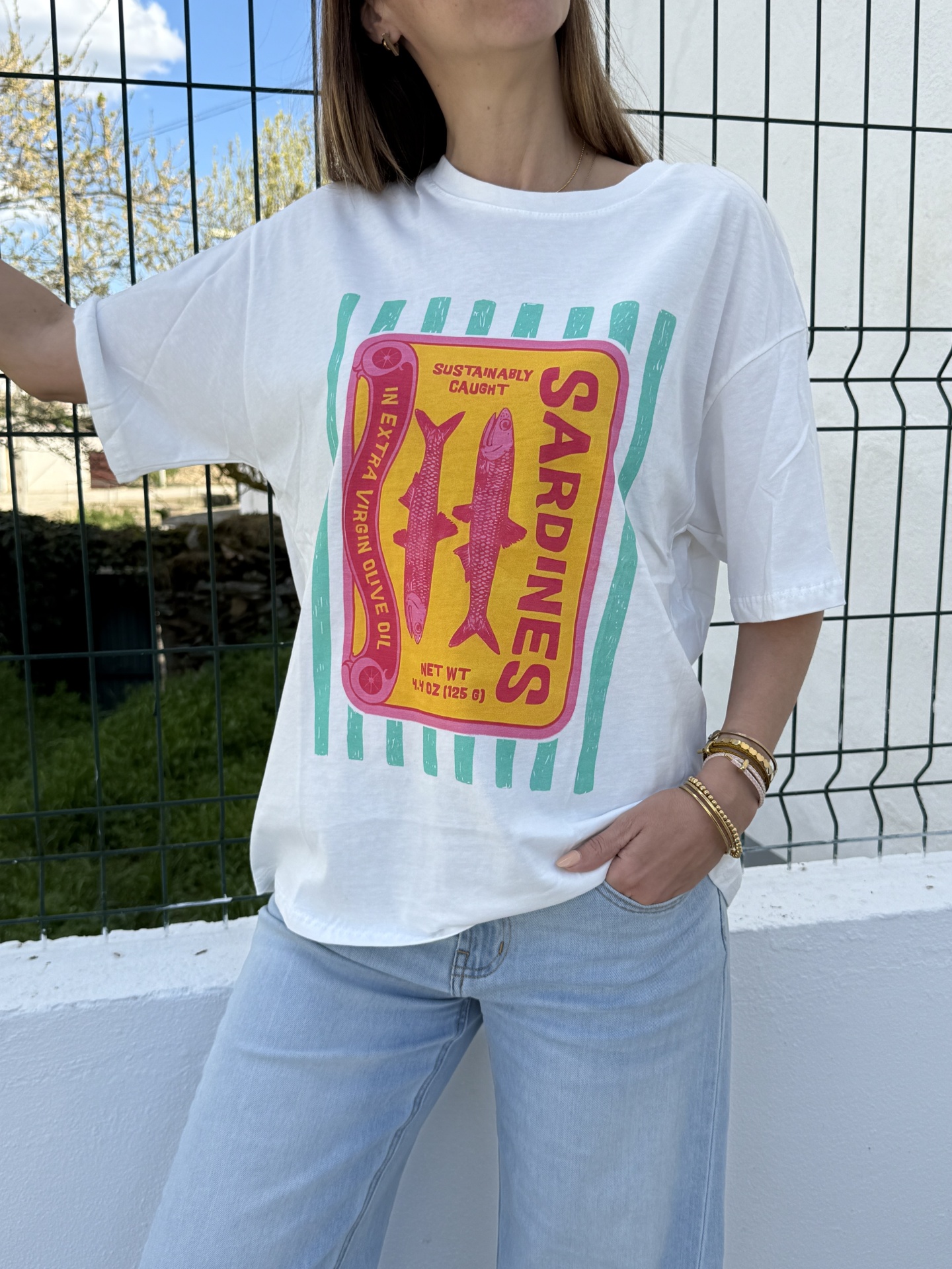 T-shirt branca com estampa colorida de caixa de sardinhas e calças de ganga azuis claras