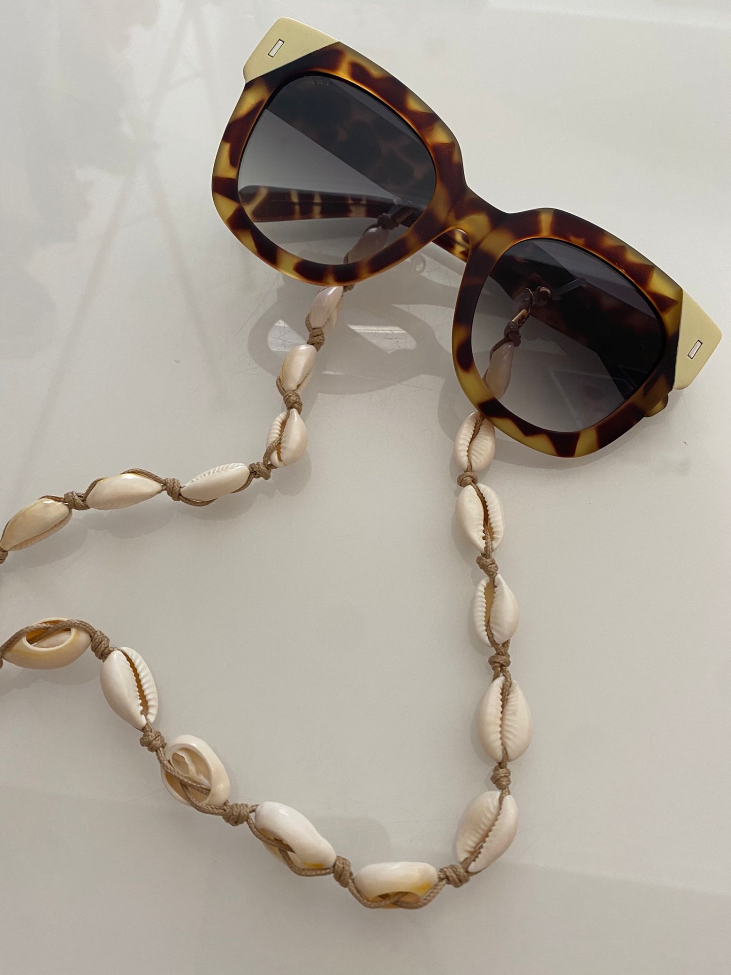 Óculos de sol com armação tartaruga e cordão de conchas em fundo branco