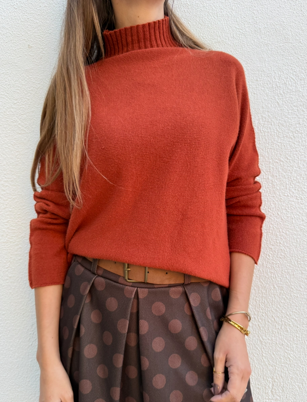 Pessoa com camisola vermelha de gola alta e saia castanha de bolinhas