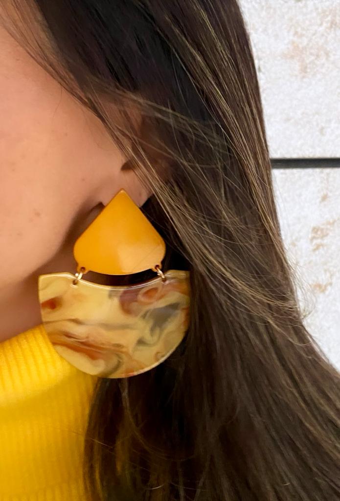 Brinco amarelo com padrão marmoreado em orelha de pessoa com cabelo castanho