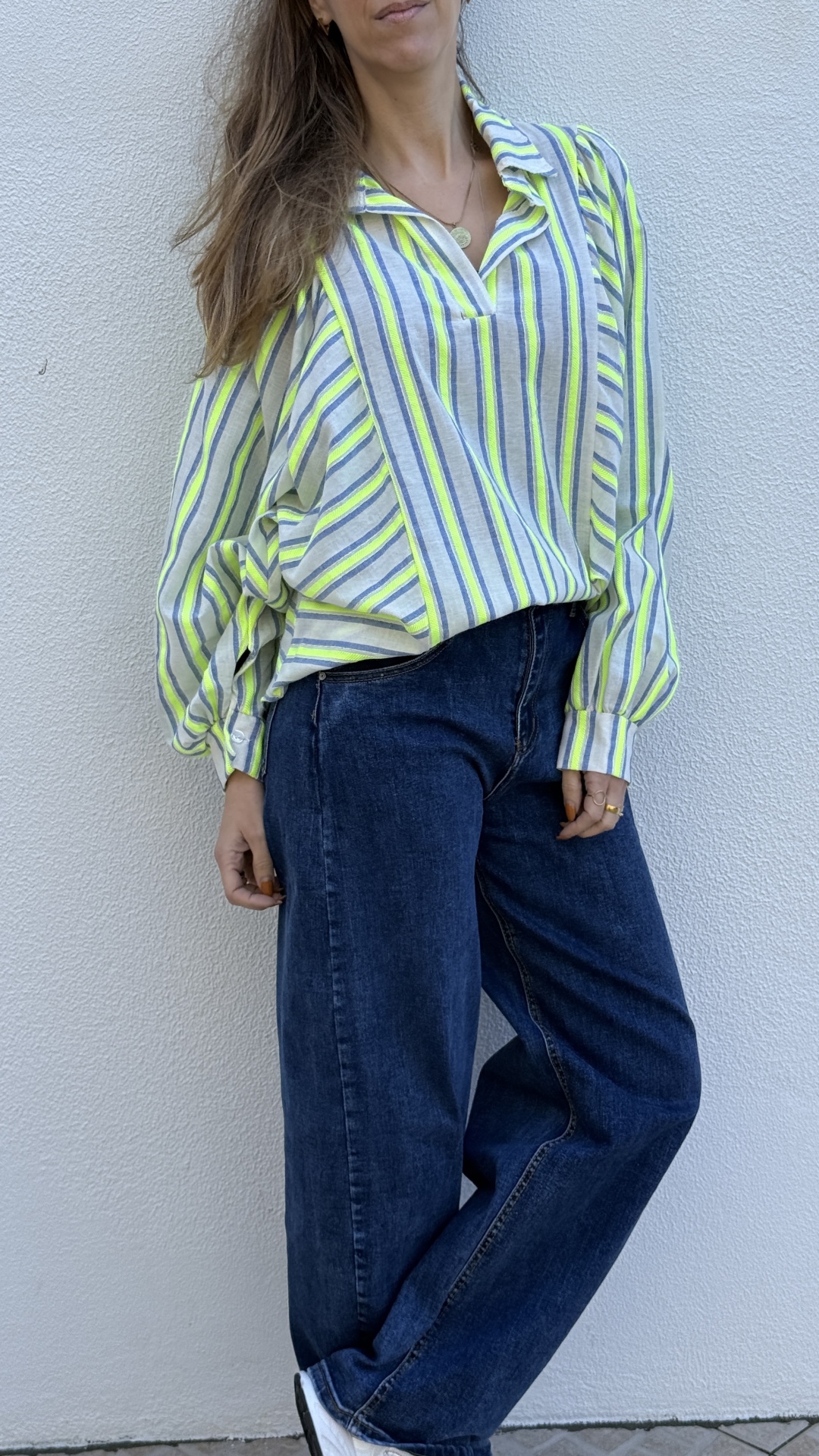 Mulher com camisa de riscas verticais verde-fluorescente e calças de ganga largas azuis