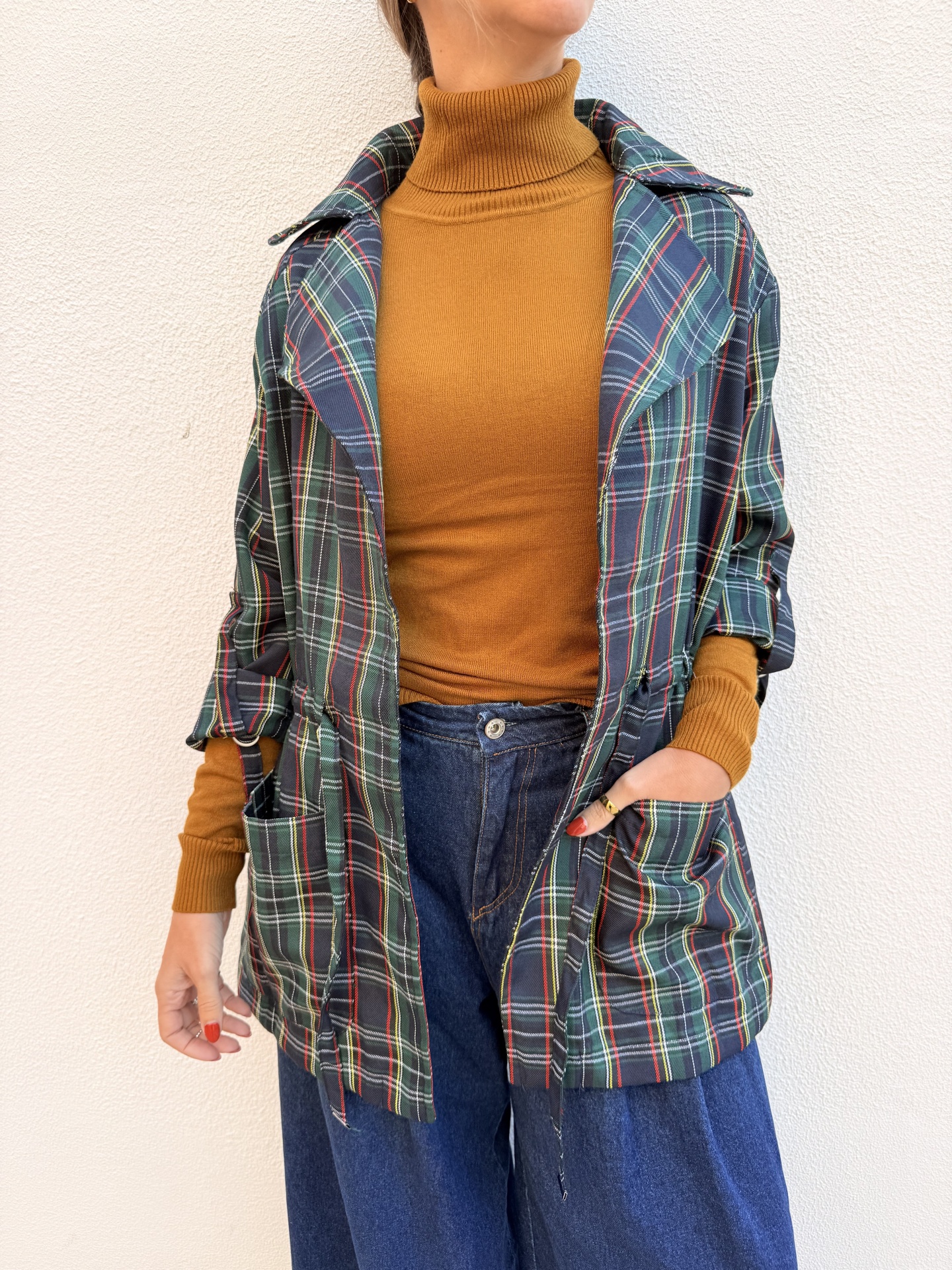 Pessoa a usar camisola castanha, casaco tartan verde e calças de ganga azuis