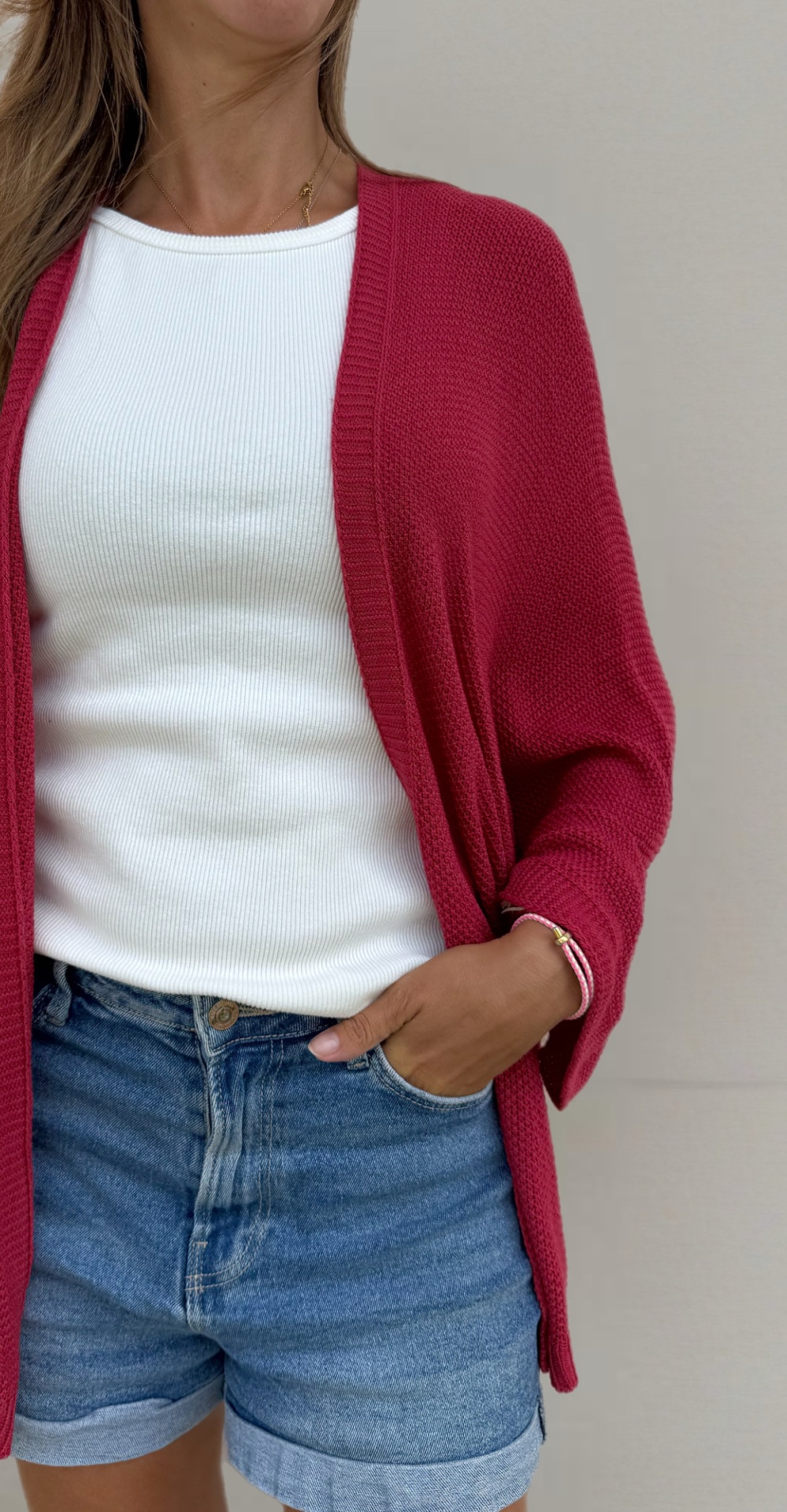 Cardigã vermelho-alaranjado malha com camisola branca e calções de ganga azuis