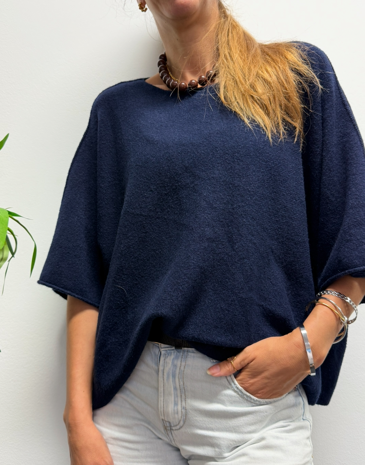 Pessoa vestindo suéter azul escuro de malha e calças claras com colar e pulseiras