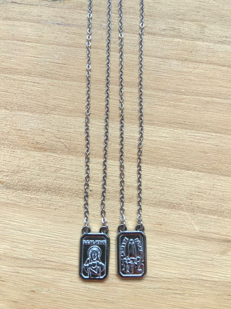 Duas correntes prateadas com pendentes retangulares de temática religiosa sobre madeira clara