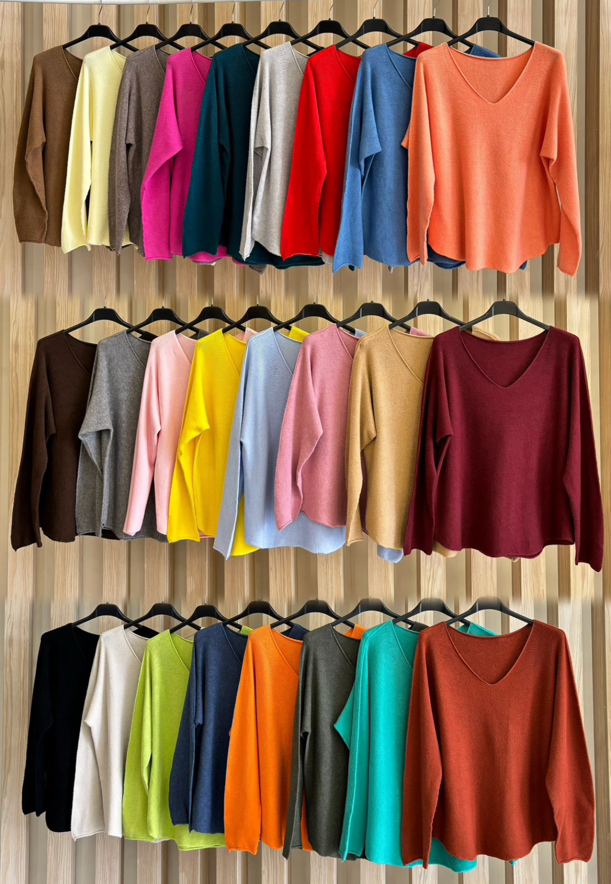 Camisolas de malha coloridas com decote em V penduradas em cabides contra parede de madeira.