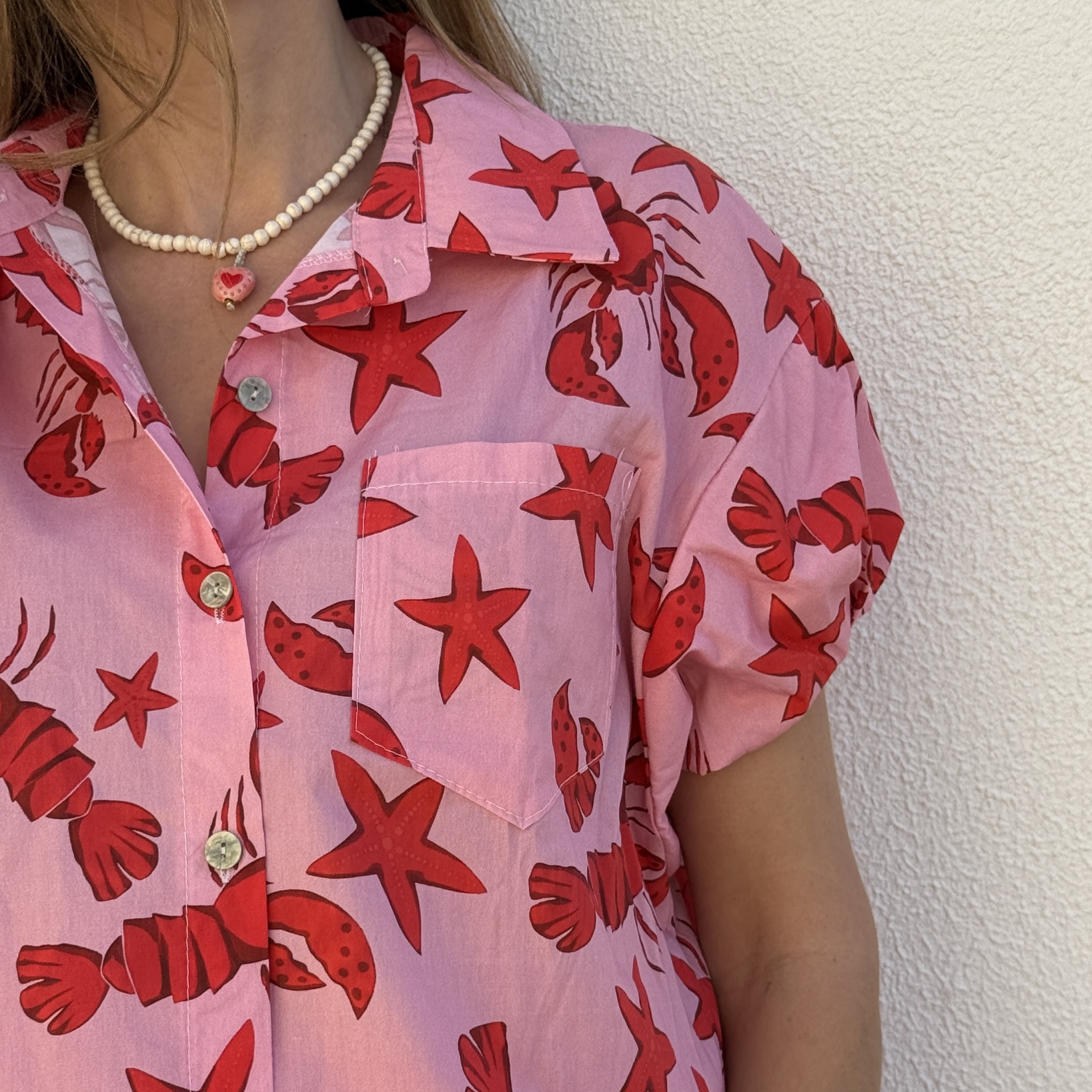 Camisa rosa de manga curta com padrão vermelho e colar de contas brancas com pendente rosa