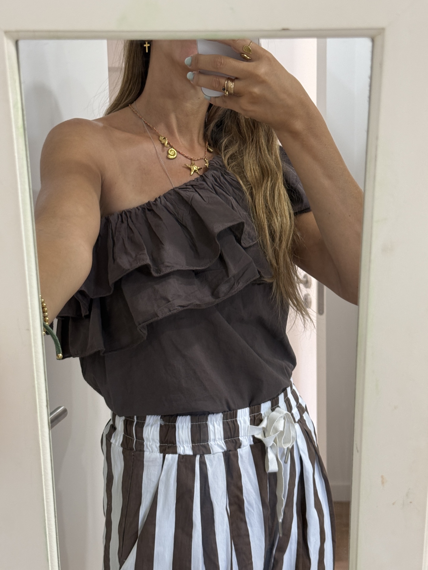 Blusa castanha com folhos e saia/calças às riscas brancas e castanhas com acessórios dourados.