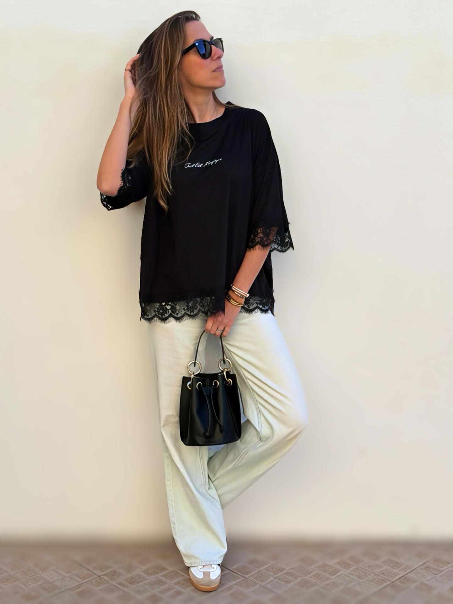Mulher com blusa preta com renda, calças brancas largas, óculos de sol e mala preta pequena.