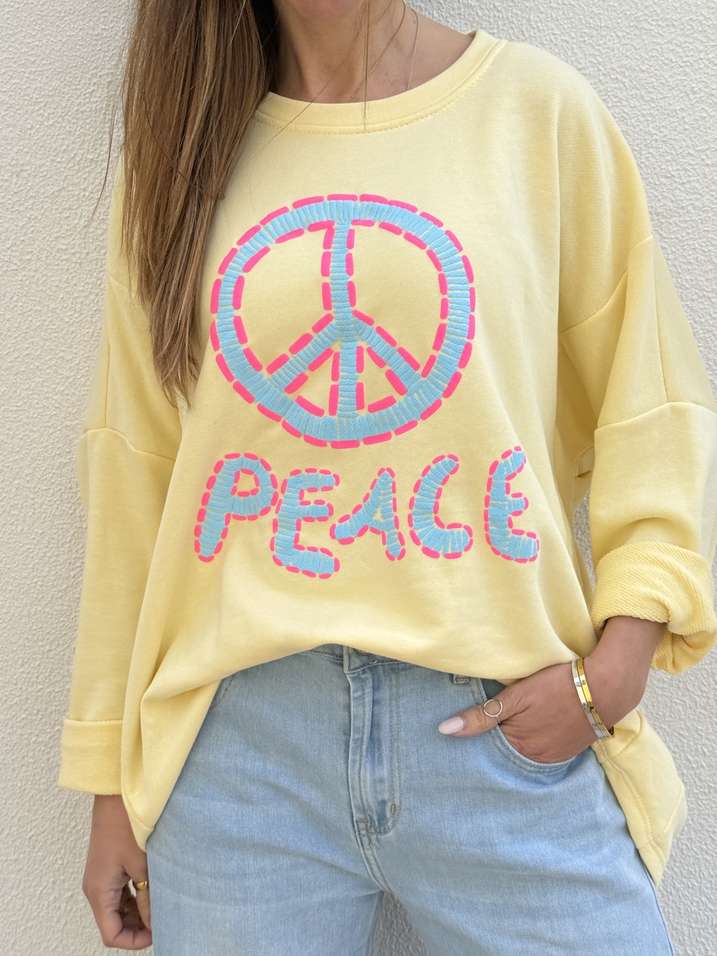 Sweatshirt amarela com estampa símbolo da paz e palavra PEACE em azul claro com contorno rosa.