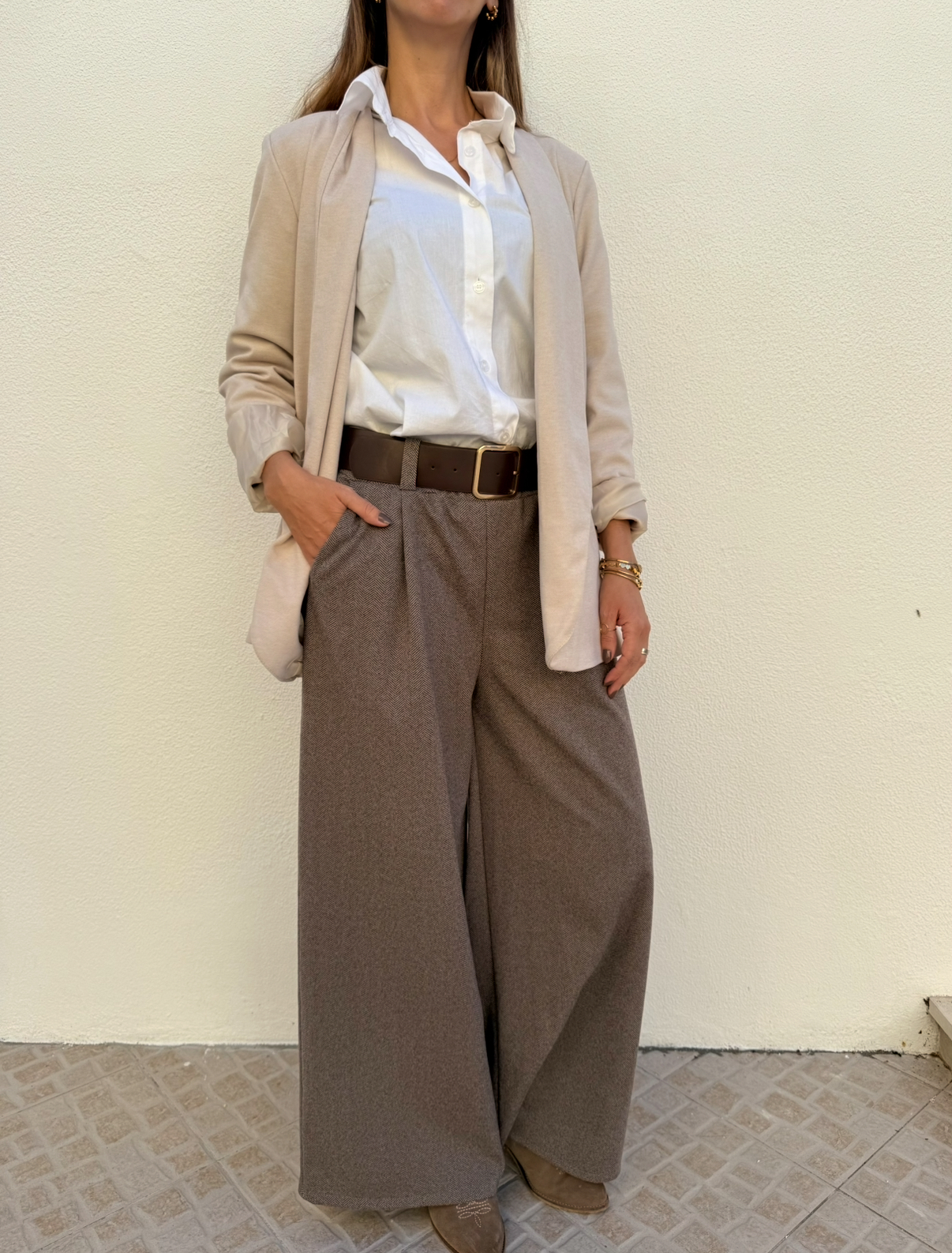 Mulher com blazer bege, camisa branca, calças largas castanhas e botas bege