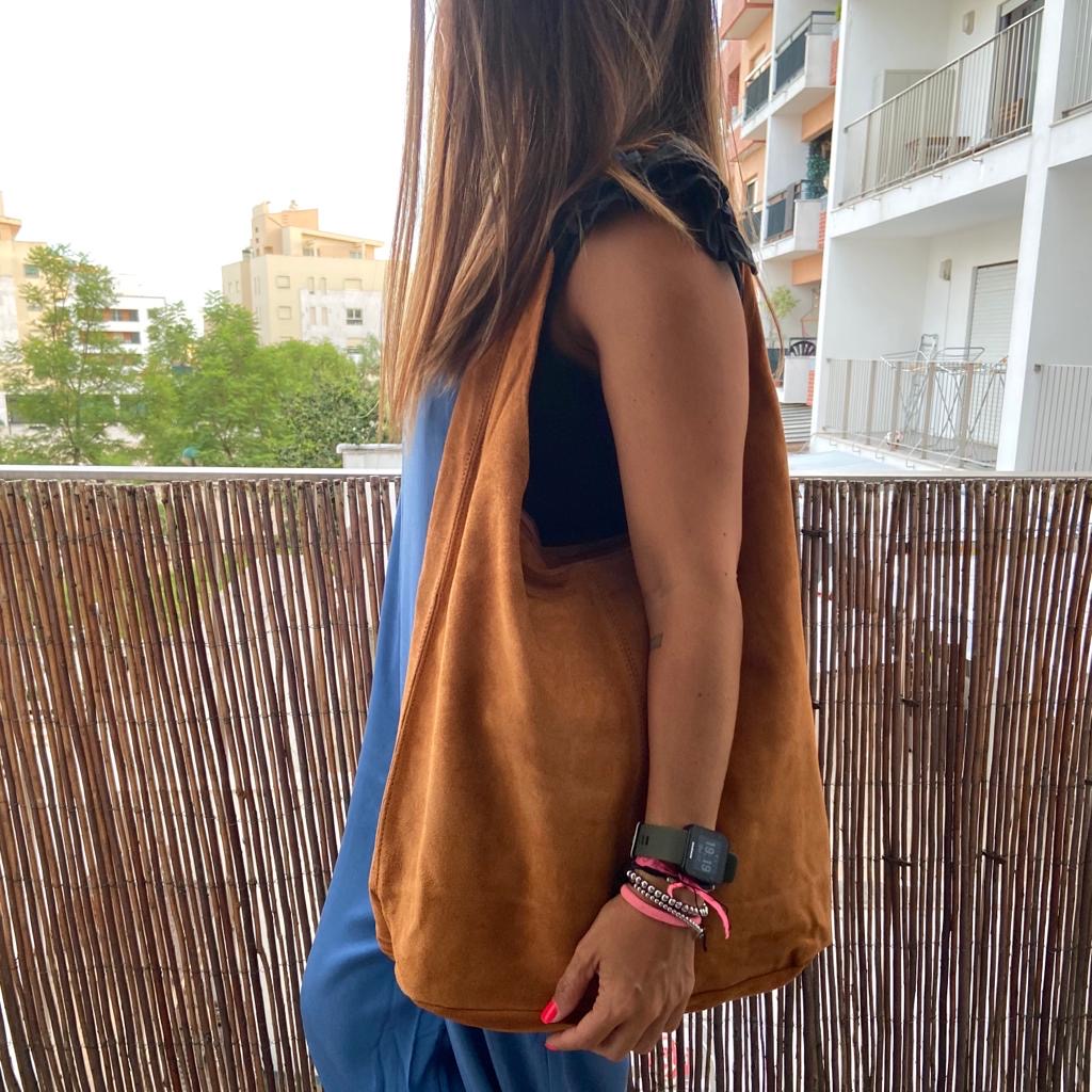 Bolsa castanha de tecido tipo camurça usada por mulher com roupa azul e preta num terraço com vedação de bambu