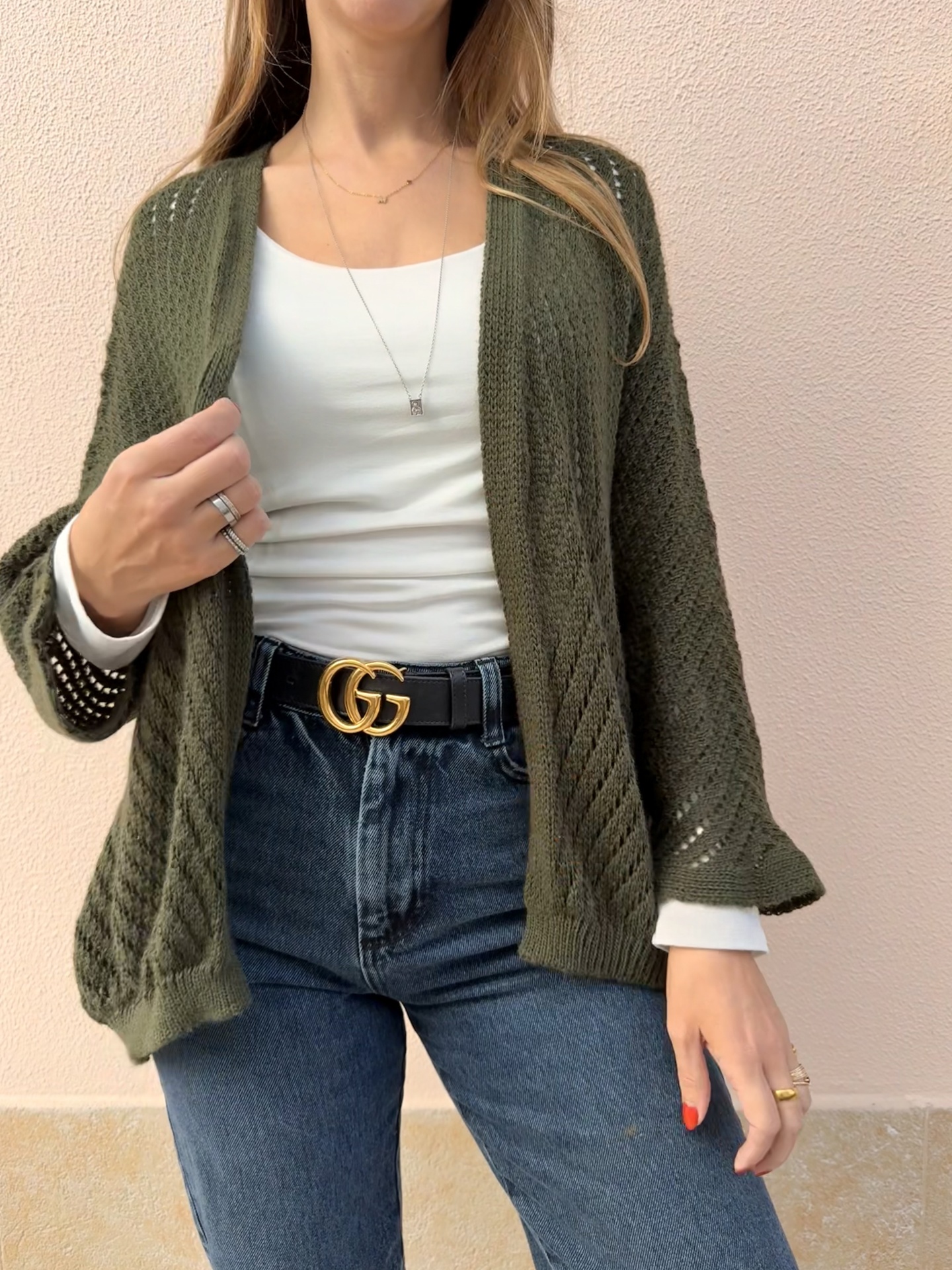Pessoa vestindo cardigan verde, camisola branca, jeans azul e cinto preto com fivela dourada GG