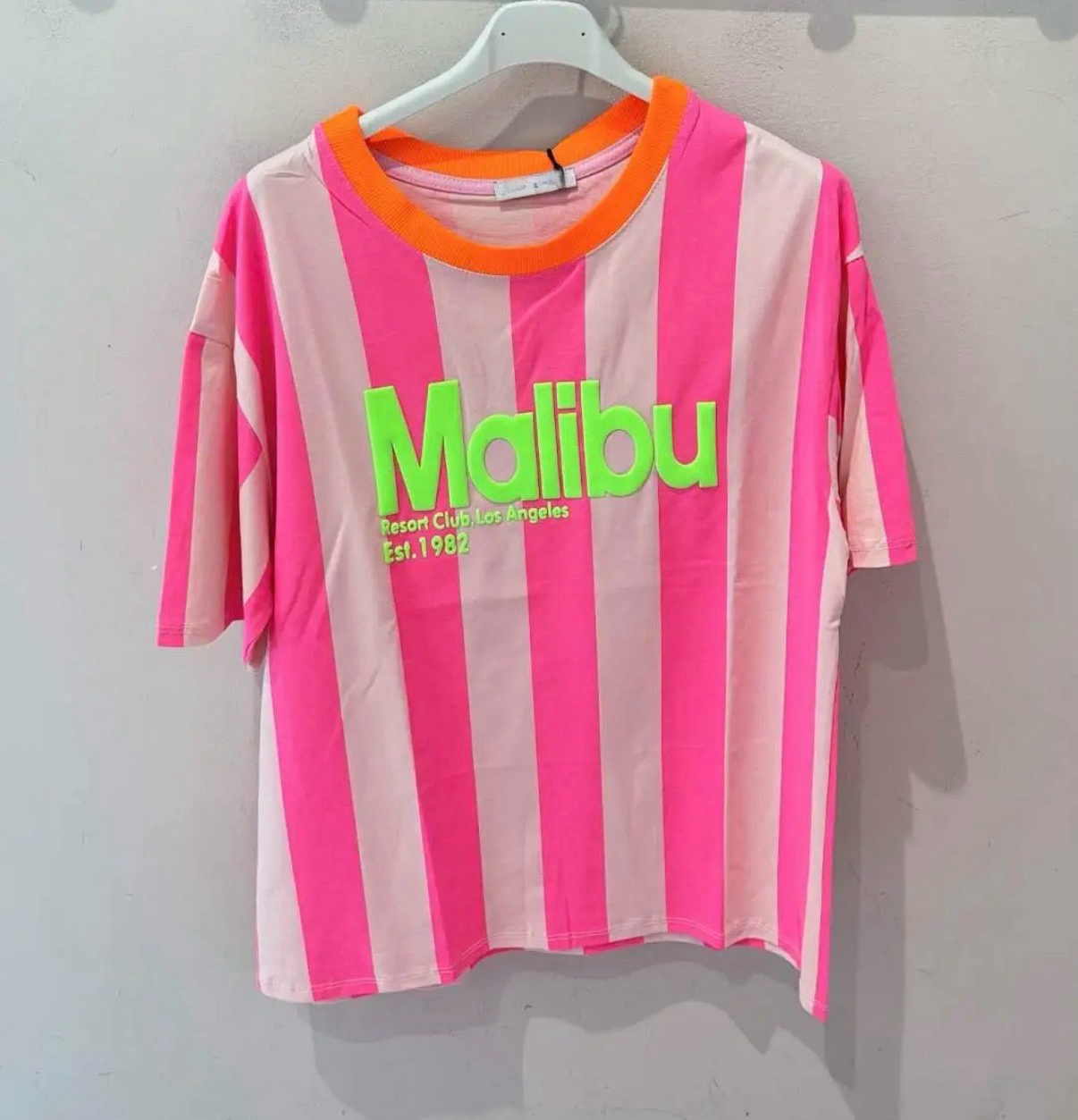 T-shirt rosa com riscas verticais e texto verde Malibu pendurada numa cabide branca