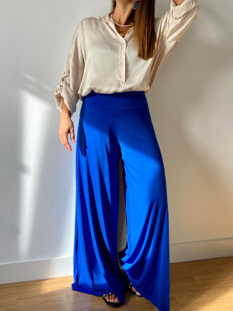 Mulher usando camisa bege e calças largas azuis em ambiente interno