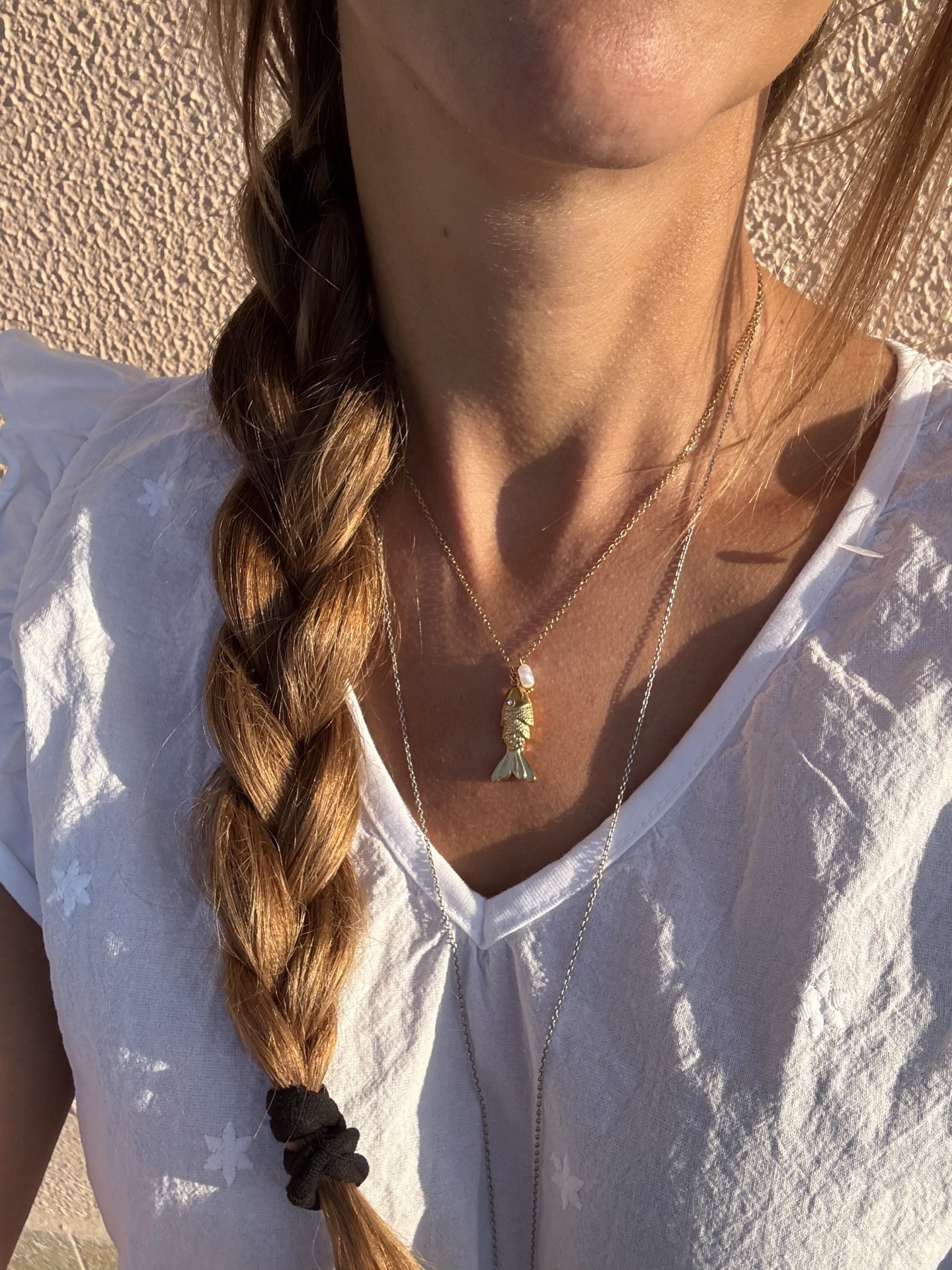 Colar com pendente de peixe em mulher com trança e t-shirt branca