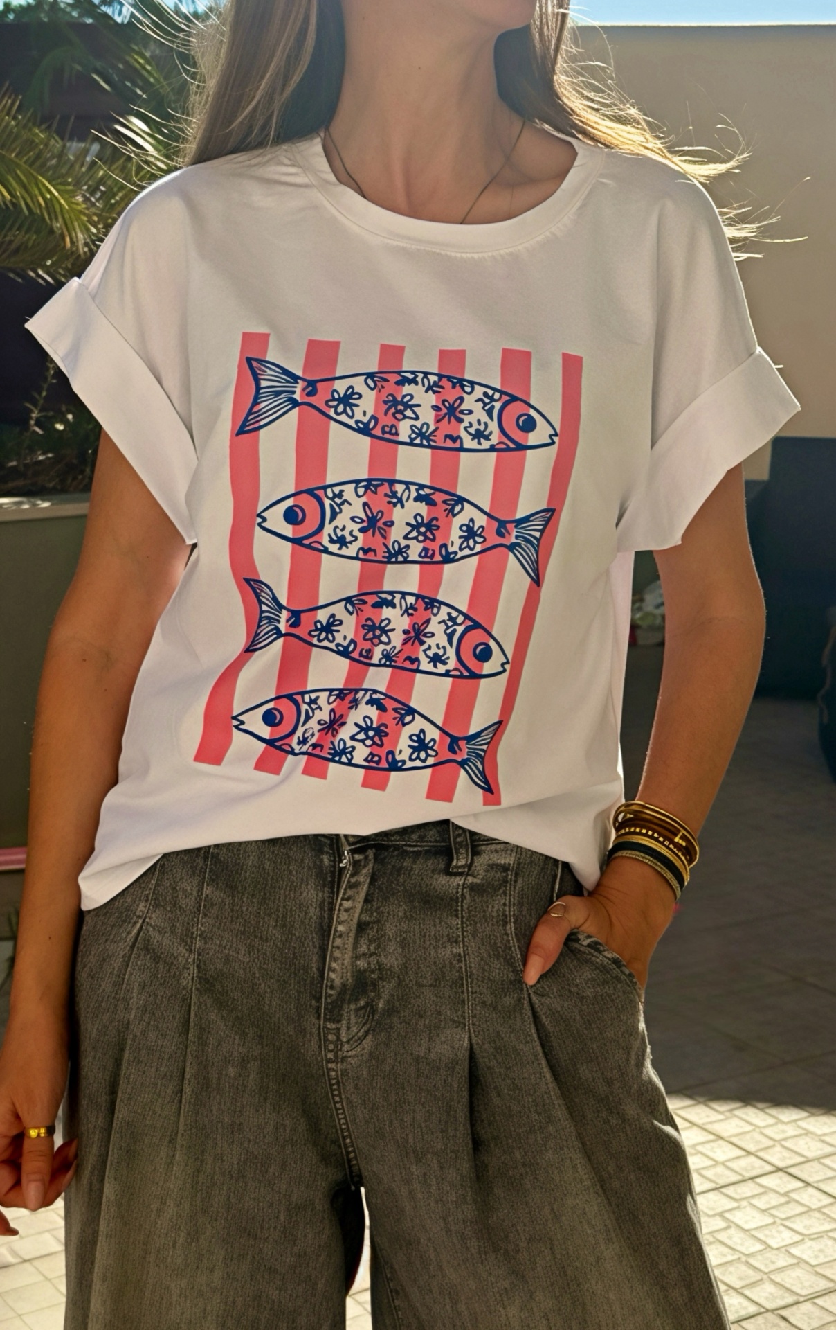 T-shirt branca com estampa de peixes azuis e riscas cor-de-rosa, usada com calças de ganga cinzentas.