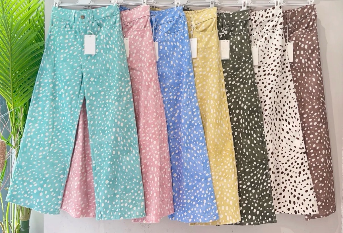 Calças compridas coloridas com padrão de bolinhas irregulares penduradas em cabide branco