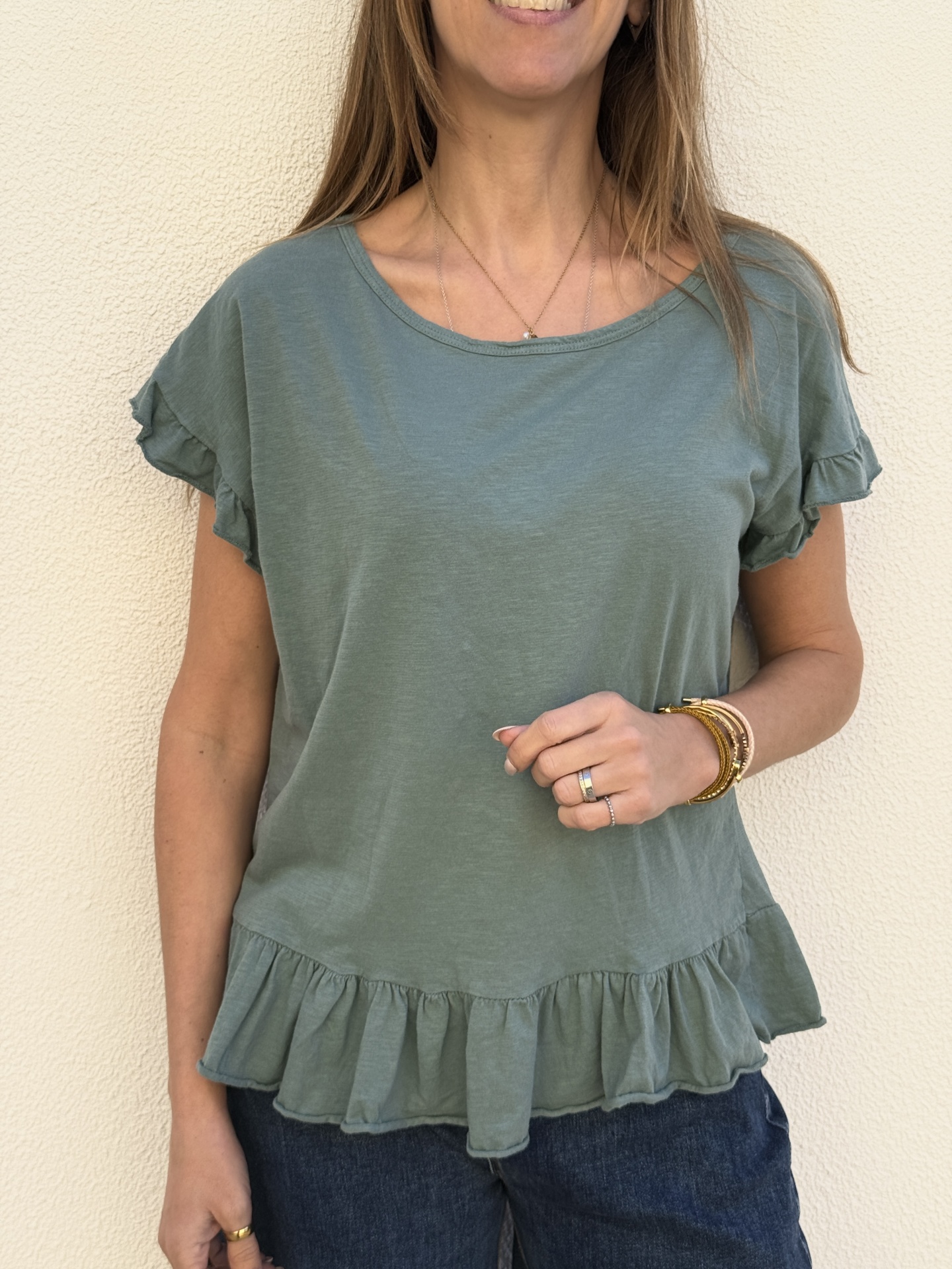 Blusa feminina verde claro com folhos na bainha e mangas, usada com calças jeans escuras.