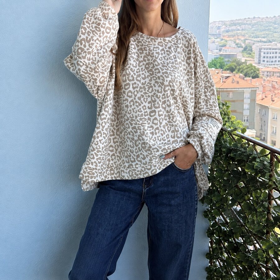 Mulher com top leopardo bege e branco e calças de ganga num ambiente de varanda