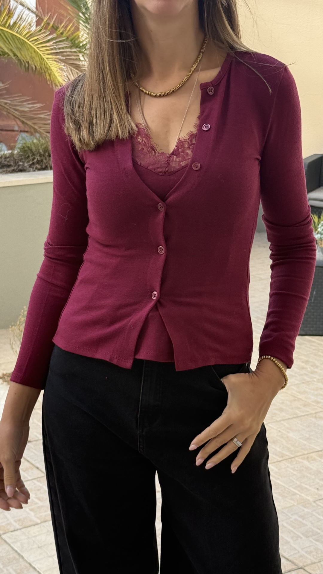 Cardigan bordô com botões usados sobre top de renda bordô e calças pretas.