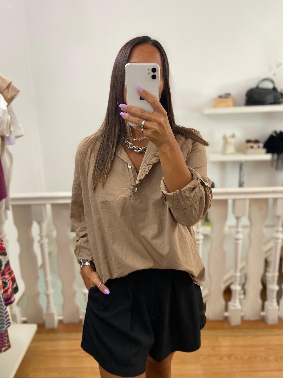 Pessoa veste blusa bege de tecido leve e saia ou calção preto em interior com móveis brancos.