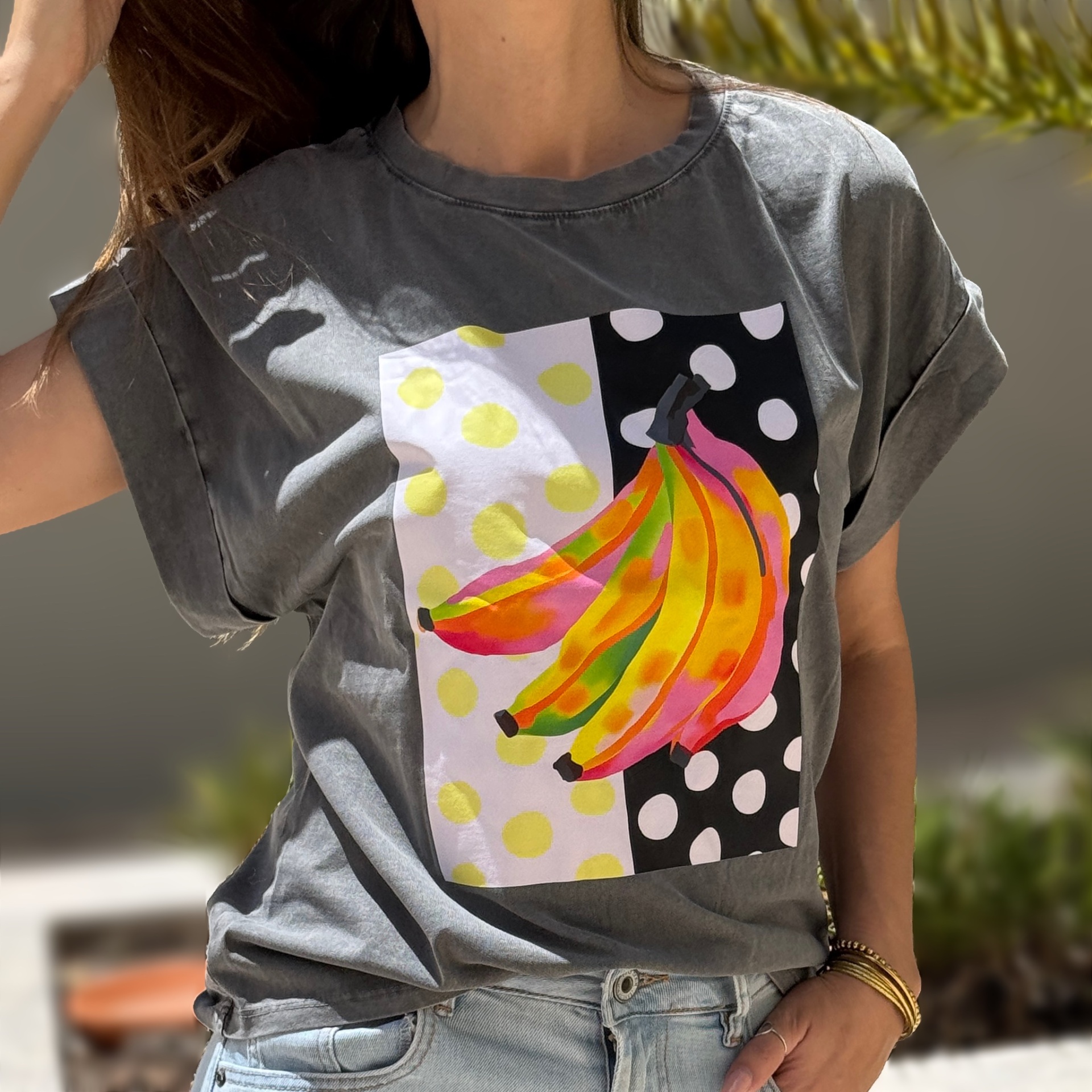 T-shirt cinzenta com estampa colorida de bananas e bolinhas, usada por pessoa com calças de ganga.