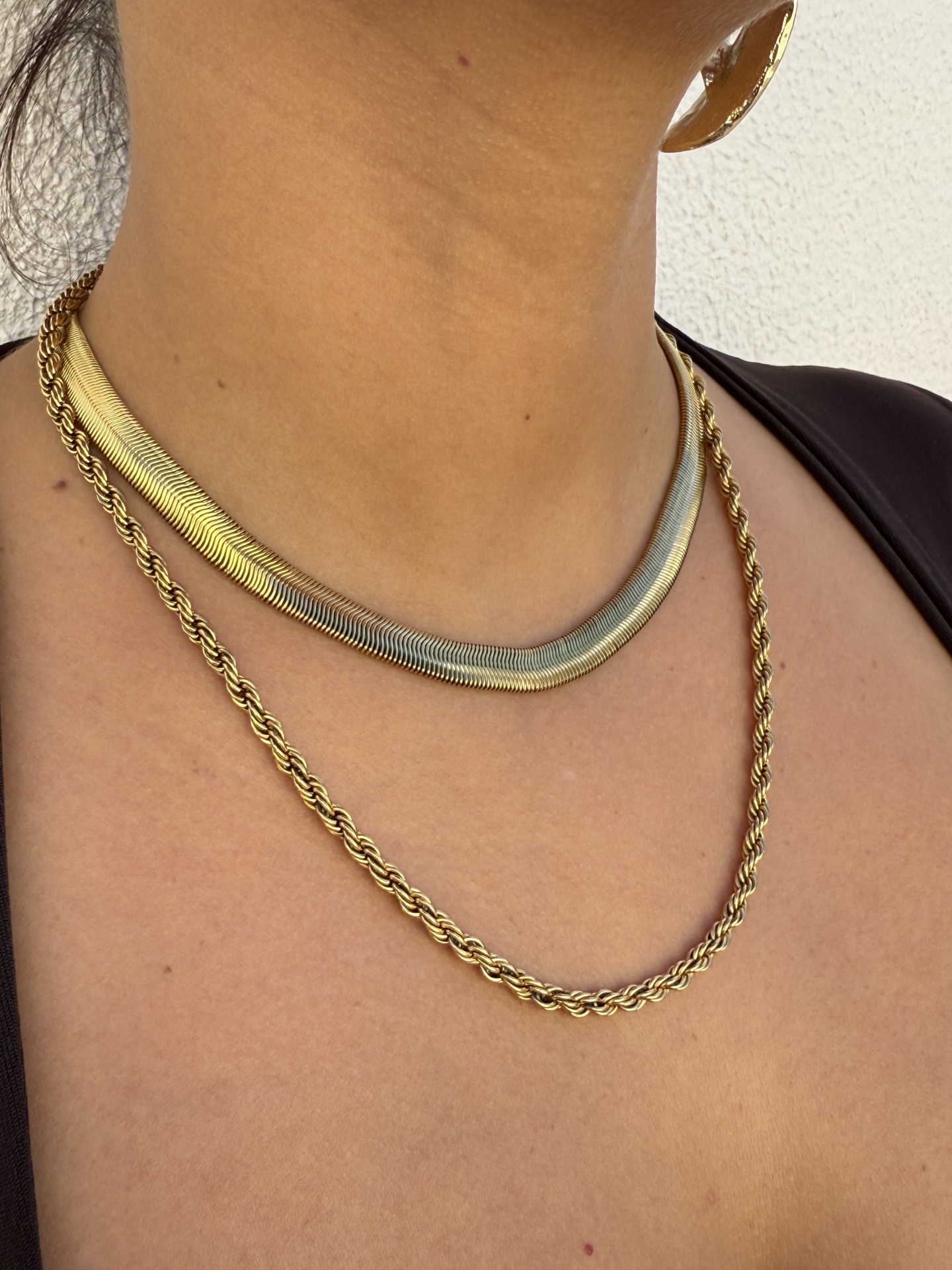 Colares dourado e prateado e brinco em argola dourada no pescoço e orelha de mulher