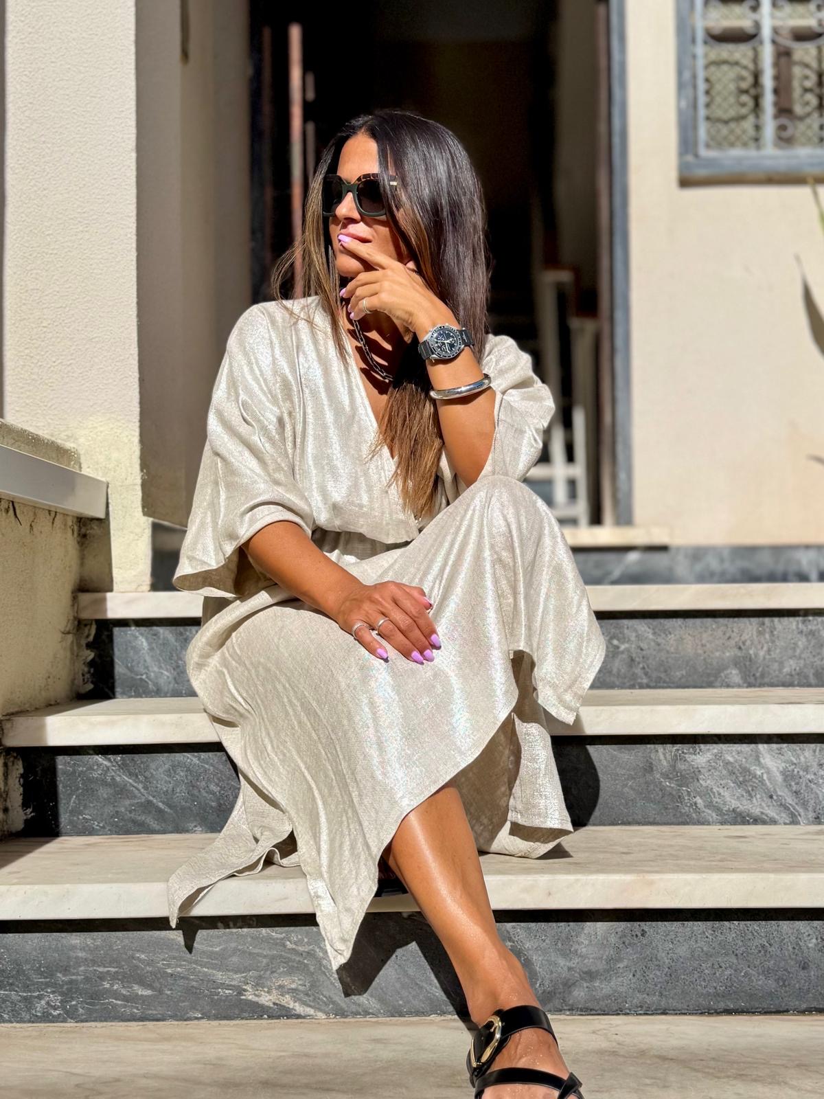 Mulher sentada em escadas, vestindo vestido branco cintilante, sandálias pretas, óculos escuros